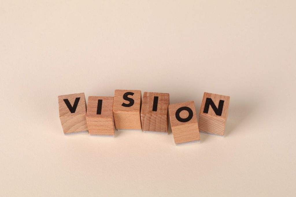 Wooden blocks with black letters spelling 'VISION' on a light beige background, symbolizing foresight and goals.